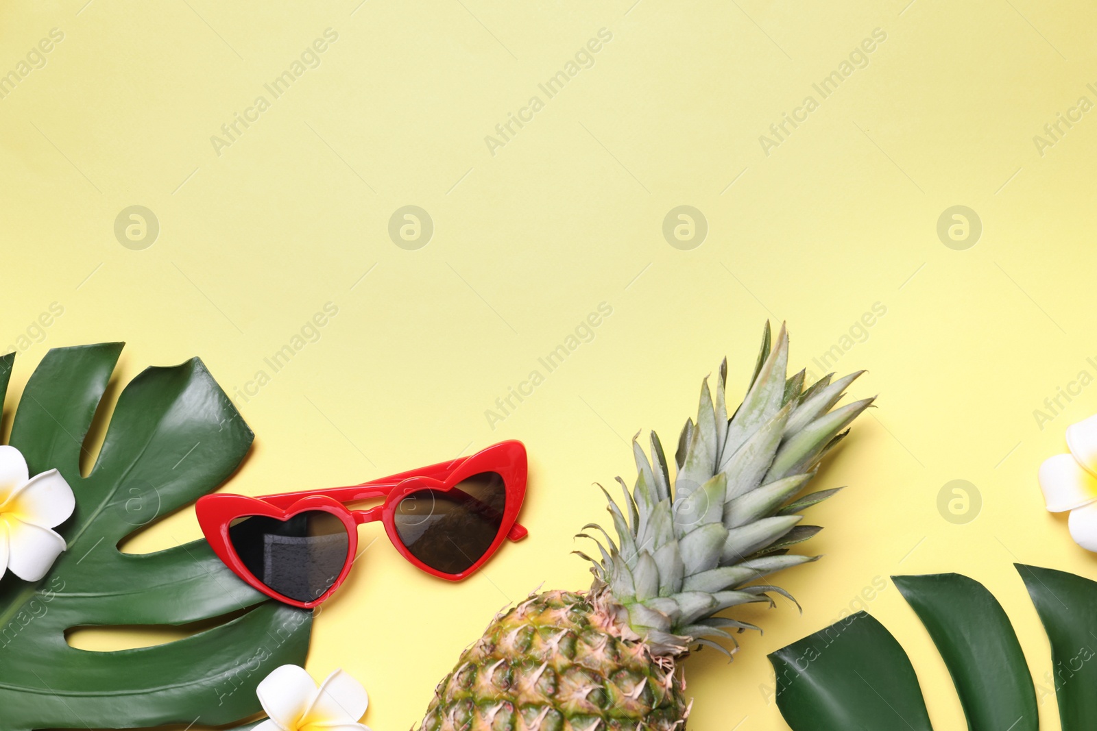 Photo of Sunglasses, fresh pineapple, tropical leaves and flowers on light yellow background, flat lay. Space for text