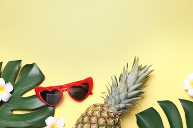 Sunglasses, fresh pineapple, tropical leaves and flowers on light yellow background, flat lay. Space for text