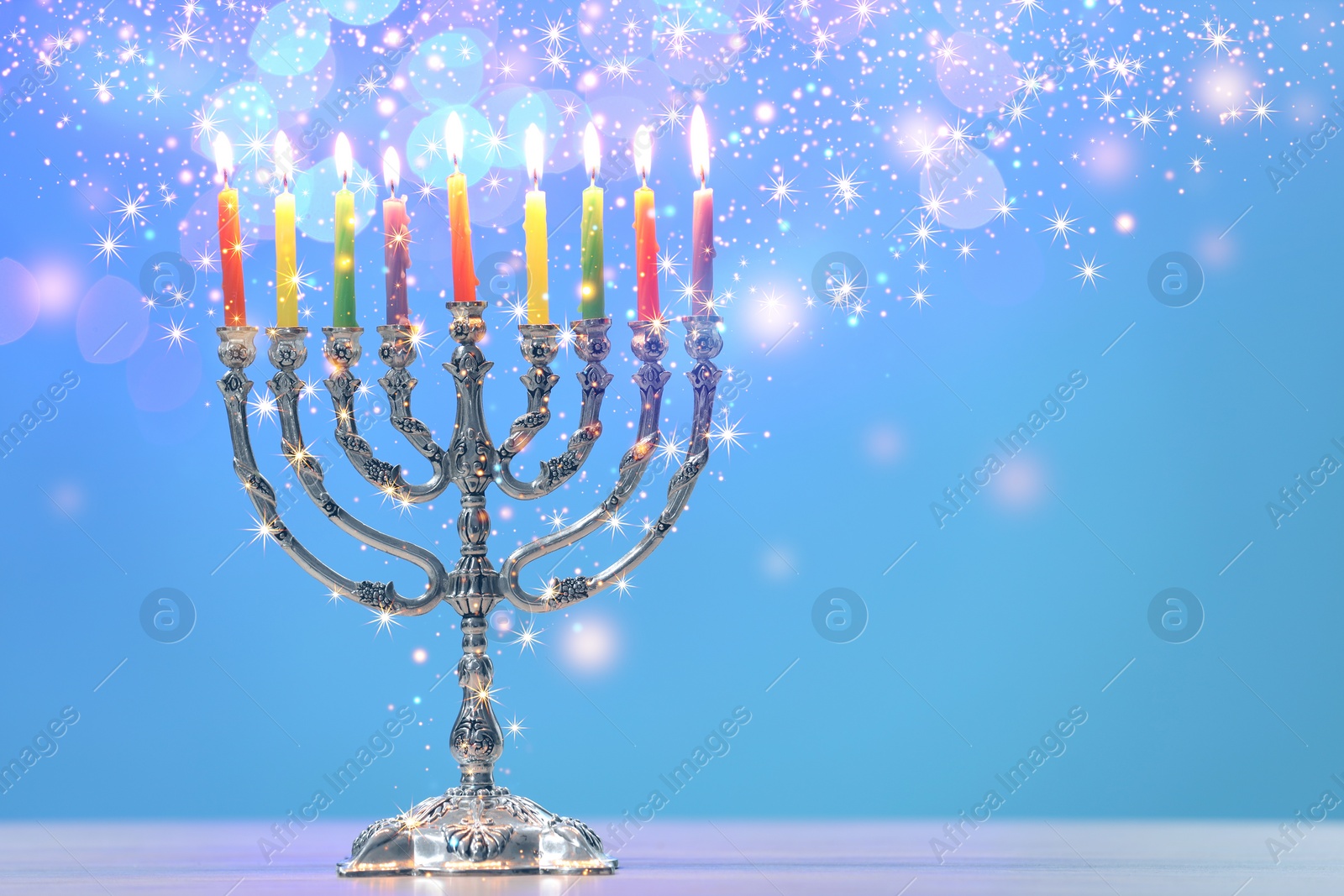 Image of Hanukkah celebration. Menorah with burning candles on table against light blue background, space for text