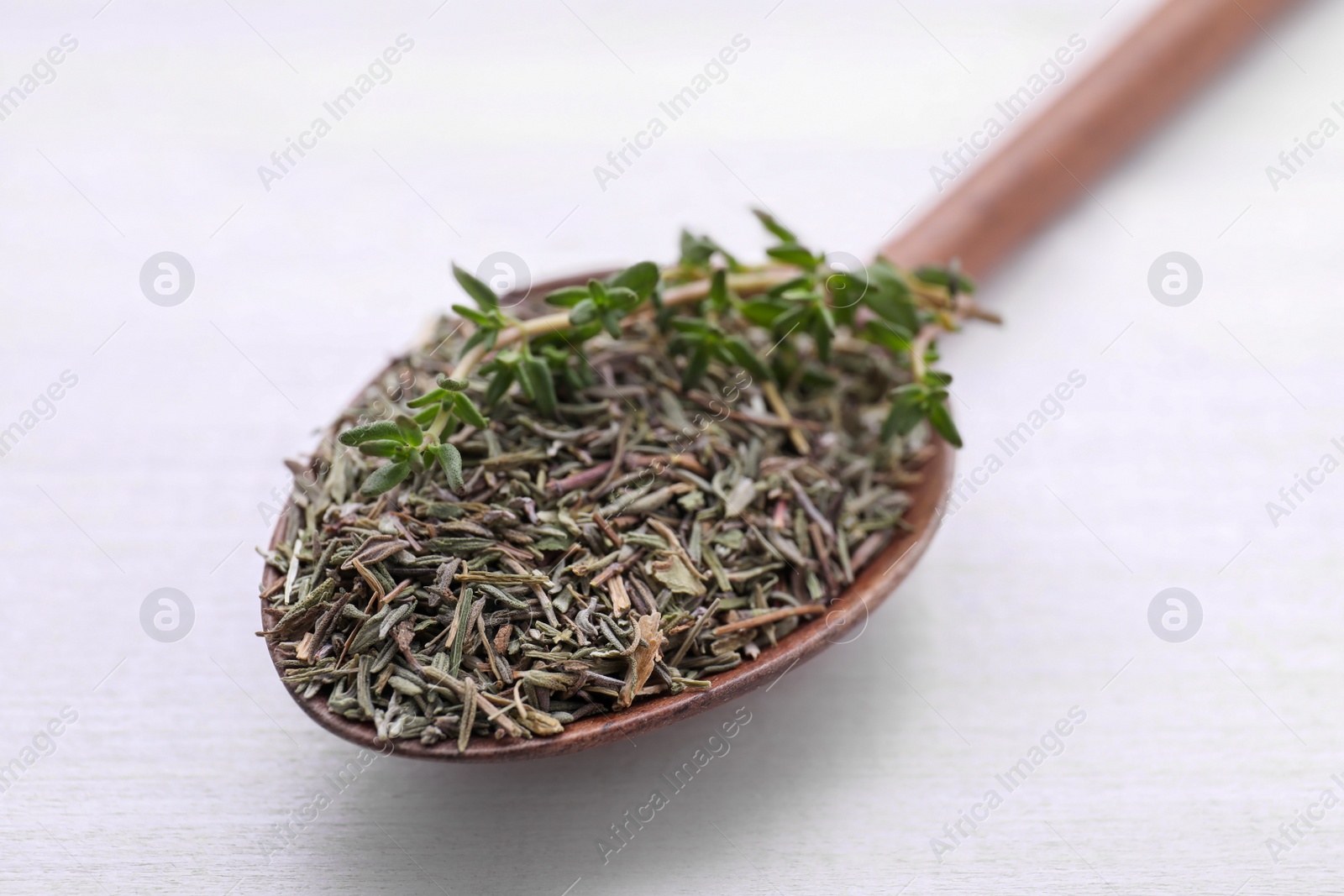 Photo of Spoon with dried thyme and fresh twig on white wooden table, closeup