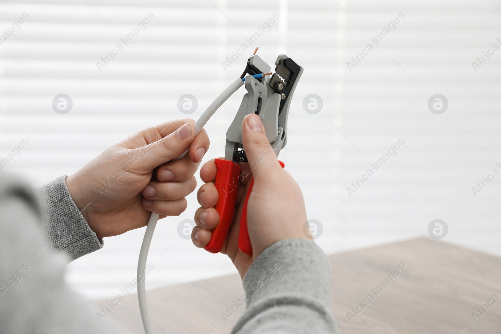 Photo of Professional electrician stripping wiring indoors, closeup view