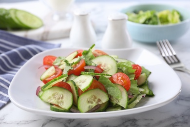 Photo of Plate of vegetarian salad with cucumber, tomato, lettuce and onion served on table, closeup