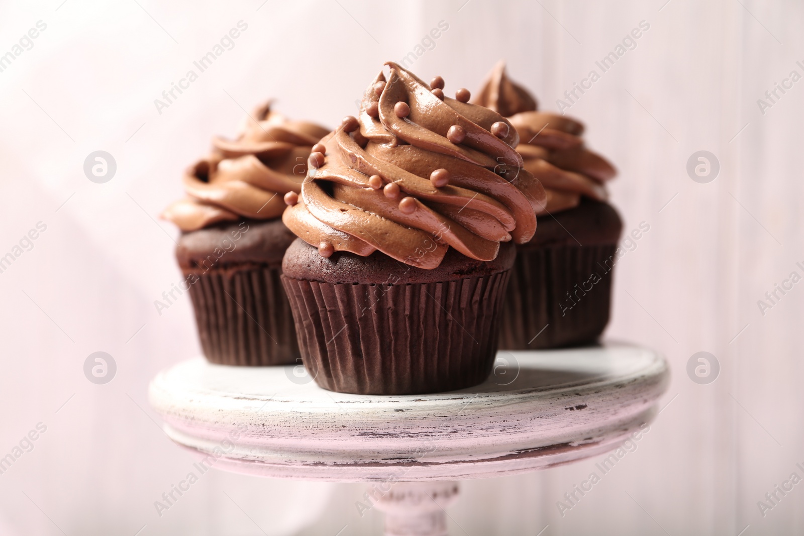 Photo of Delicious chocolate cupcakes with cream and beads on white stand, closeup