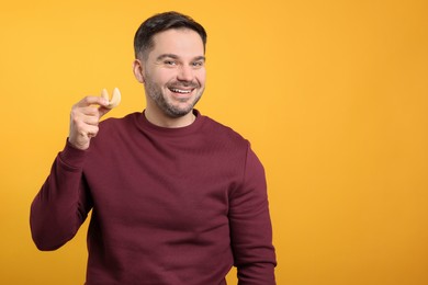 Happy man holding tasty fortune cookie with prediction on orange background. Space for text