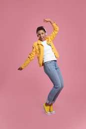 Photo of Happy young woman in headphones dancing on pink background