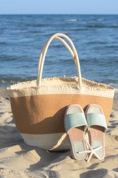 Photo of Straw bag, slippers and dry starfish on sandy beach near sea