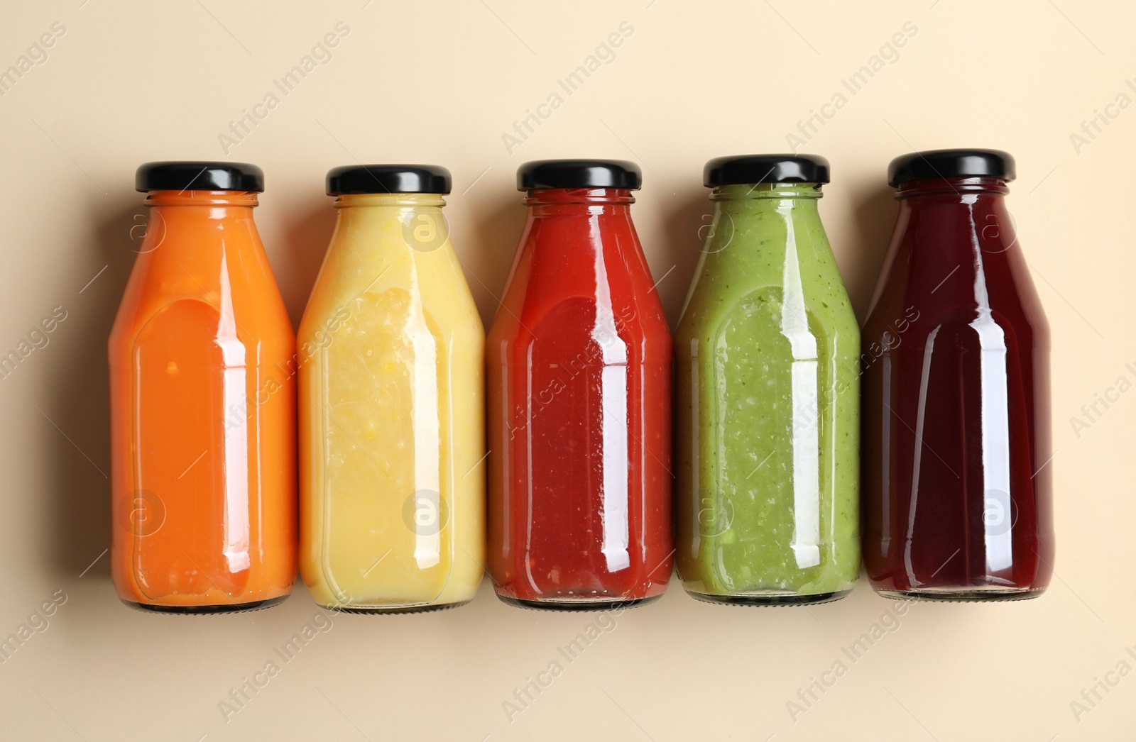 Photo of Bottles with delicious colorful juices on beige background, flat lay