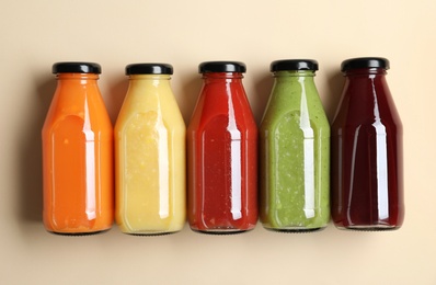 Bottles with delicious colorful juices on beige background, flat lay