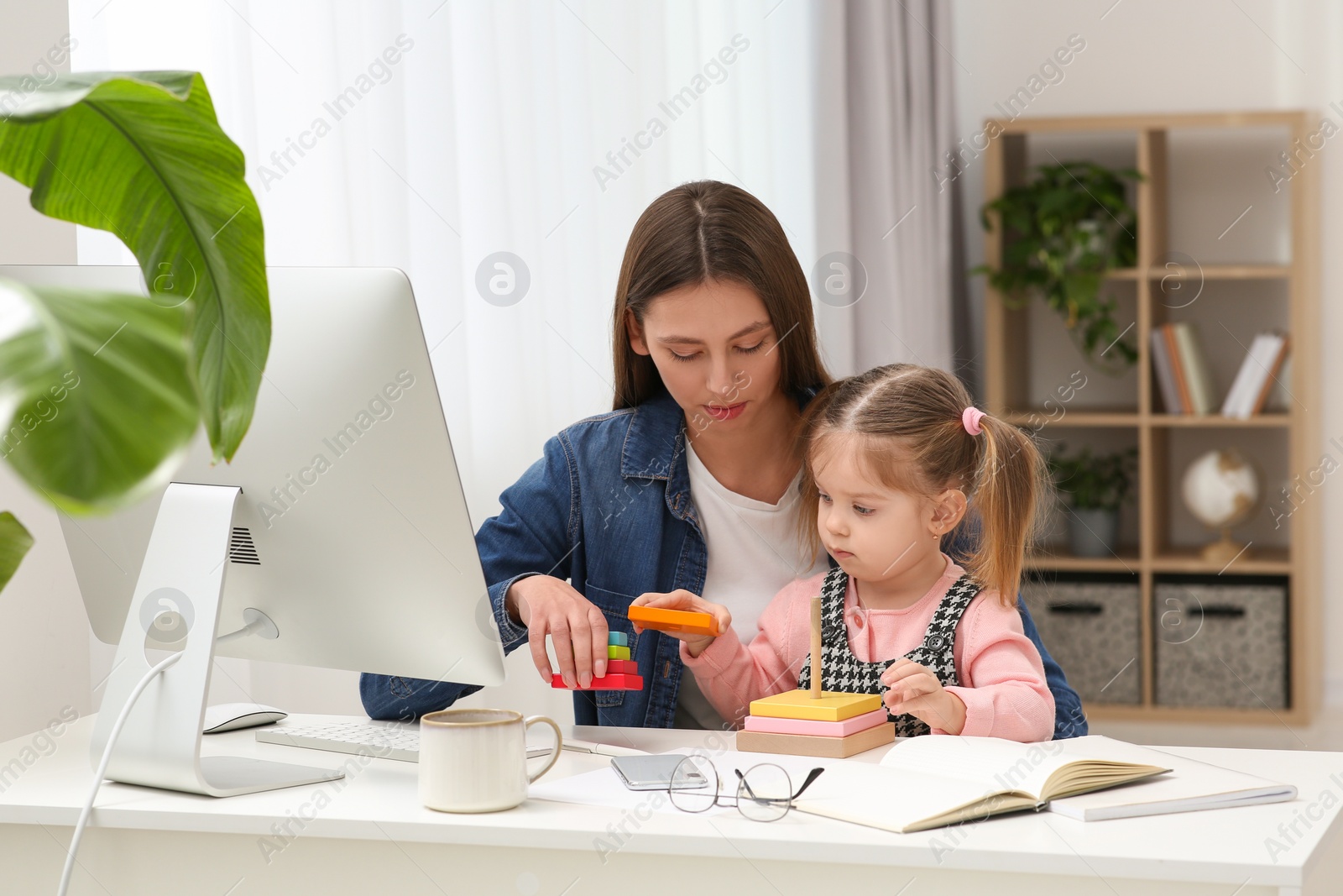 Photo of Mother playing with her daughter at desk. Taking break in remote work at home