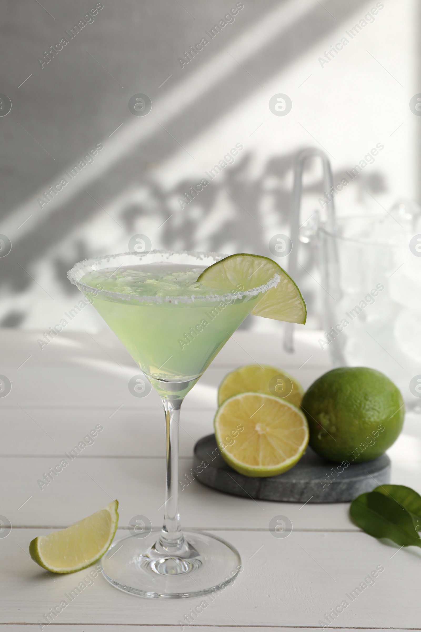 Photo of Delicious Margarita cocktail in glass and limes on white wooden table