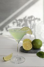 Photo of Delicious Margarita cocktail in glass and limes on white wooden table