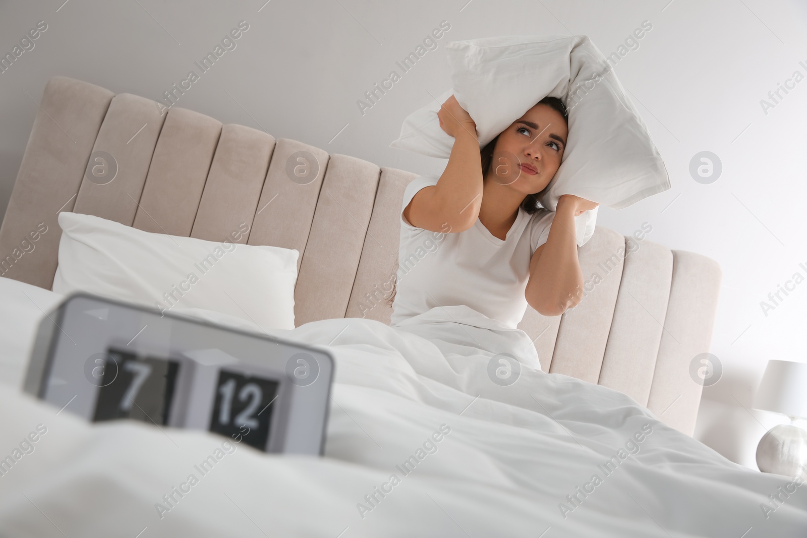 Photo of Unhappy young woman covering ears with pillow in bed at home. Noisy neighbours