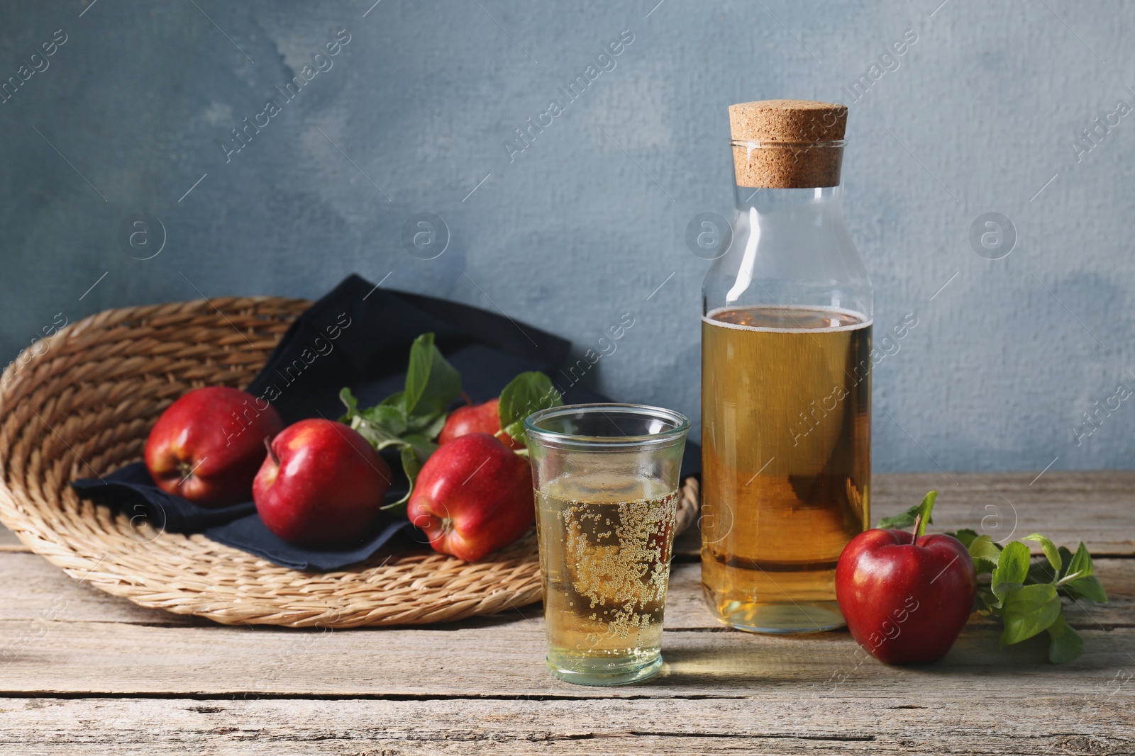 Photo of Delicious cider and red apples with green leaves on wooden table