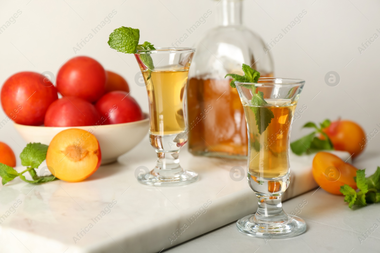 Photo of Delicious plum liquor with mint and ripe fruits on light table. Homemade strong alcoholic beverage