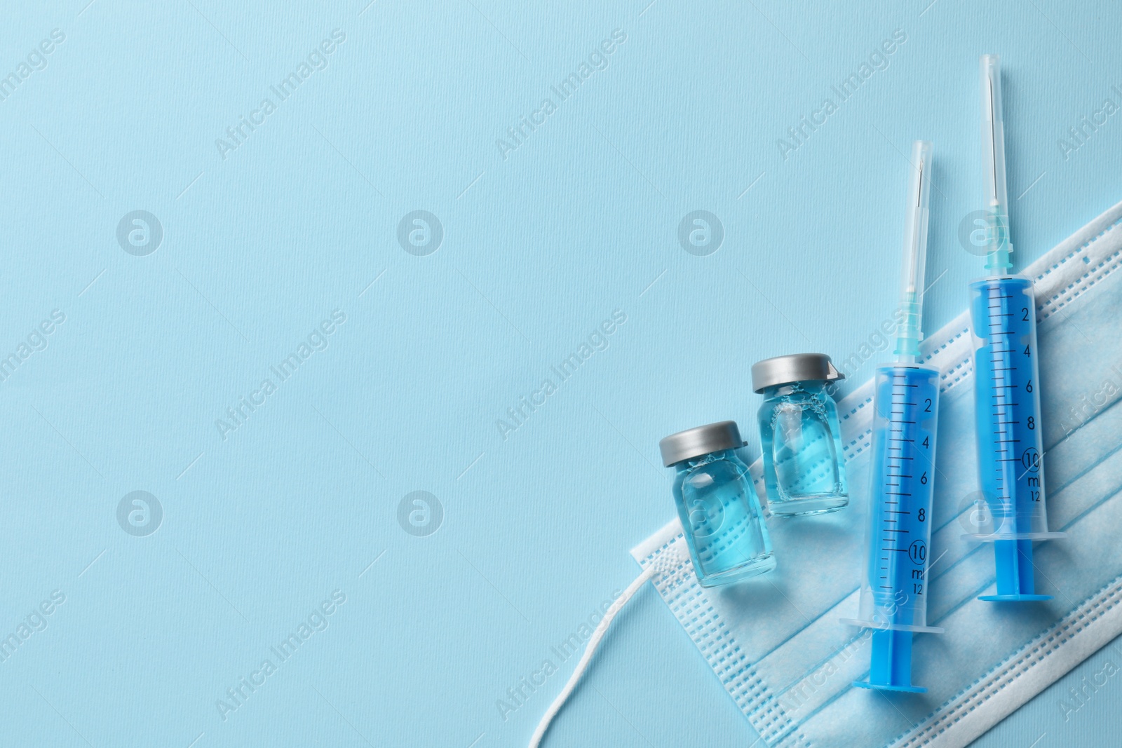 Photo of Disposable syringes with needles, protective mask and vials on light blue background, flat lay. Space for text