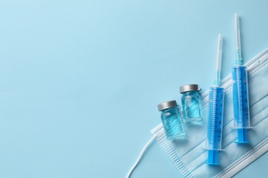 Photo of Disposable syringes with needles, protective mask and vials on light blue background, flat lay. Space for text