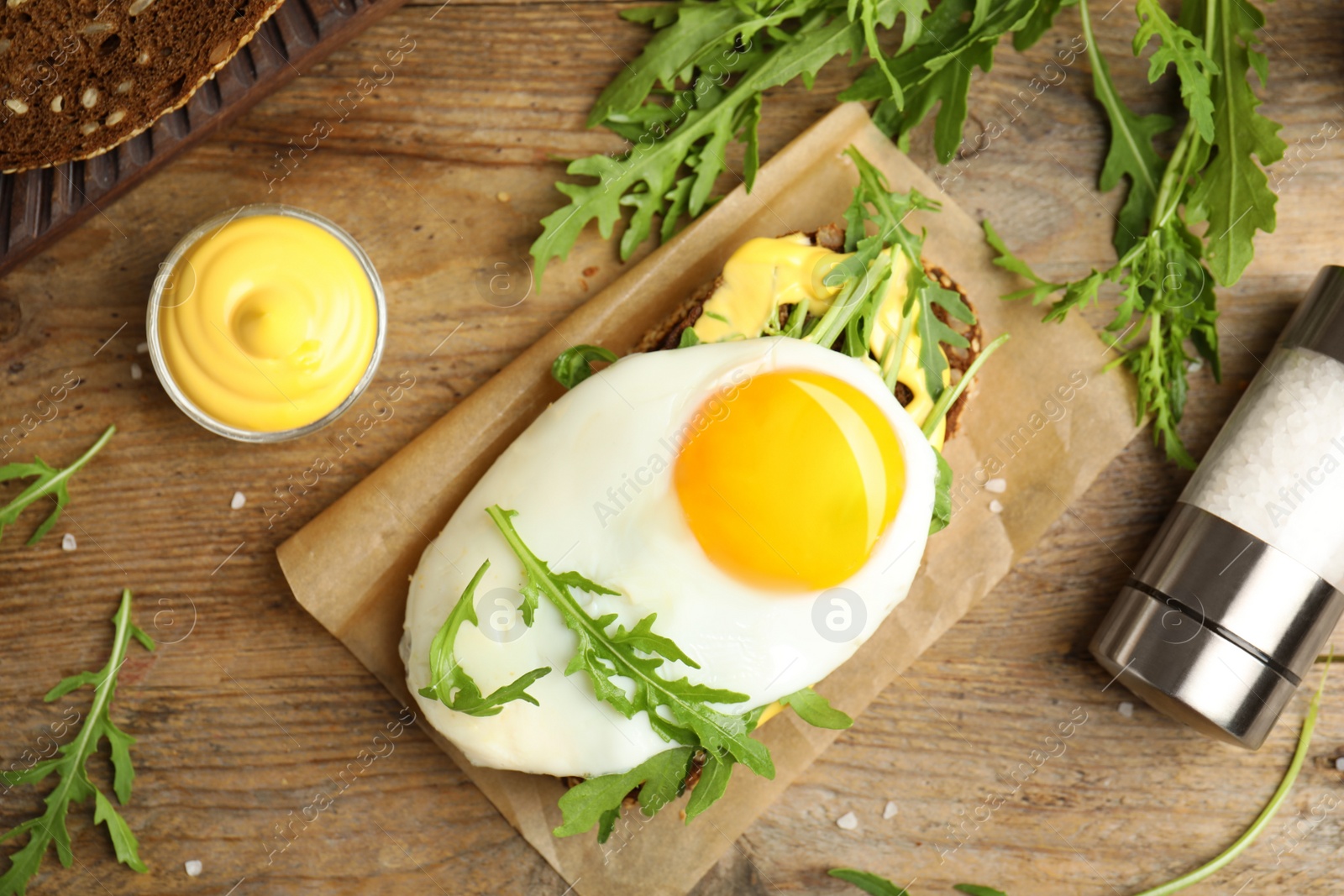 Photo of Delicious sandwich with arugula and fried egg on wooden table, flat lay