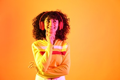 Photo of Beautiful young woman listening to music with headphones on color background in neon lights. Space for text