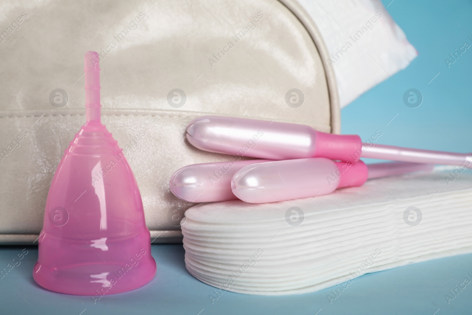 Photo of Bag with menstrual pads and other hygiene products on light blue background, closeup