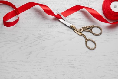 Photo of Pair of scissors with red satin ribbon on white wooden table, flat lay. Space for text