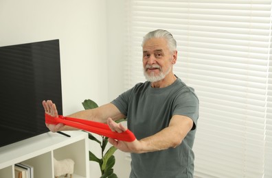 Photo of Senior man doing exercise with fitness elastic band at home