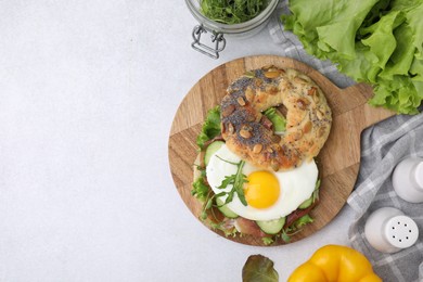 Photo of Tasty bagel with cured ham, egg, cucumber and salad mix on light table, flat lay. Space for text