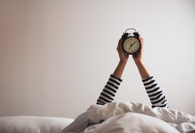 Closeup view of woman with alarm clock lying in bed, space for text. Morning time