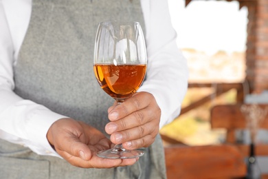 Photo of Waiter holding glass of wine in outdoor cafe, closeup