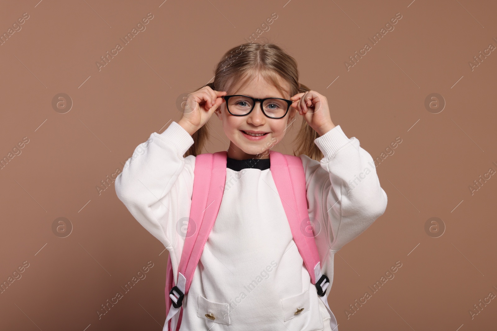 Photo of Happy schoolgirl in glasses with backpack on brown background