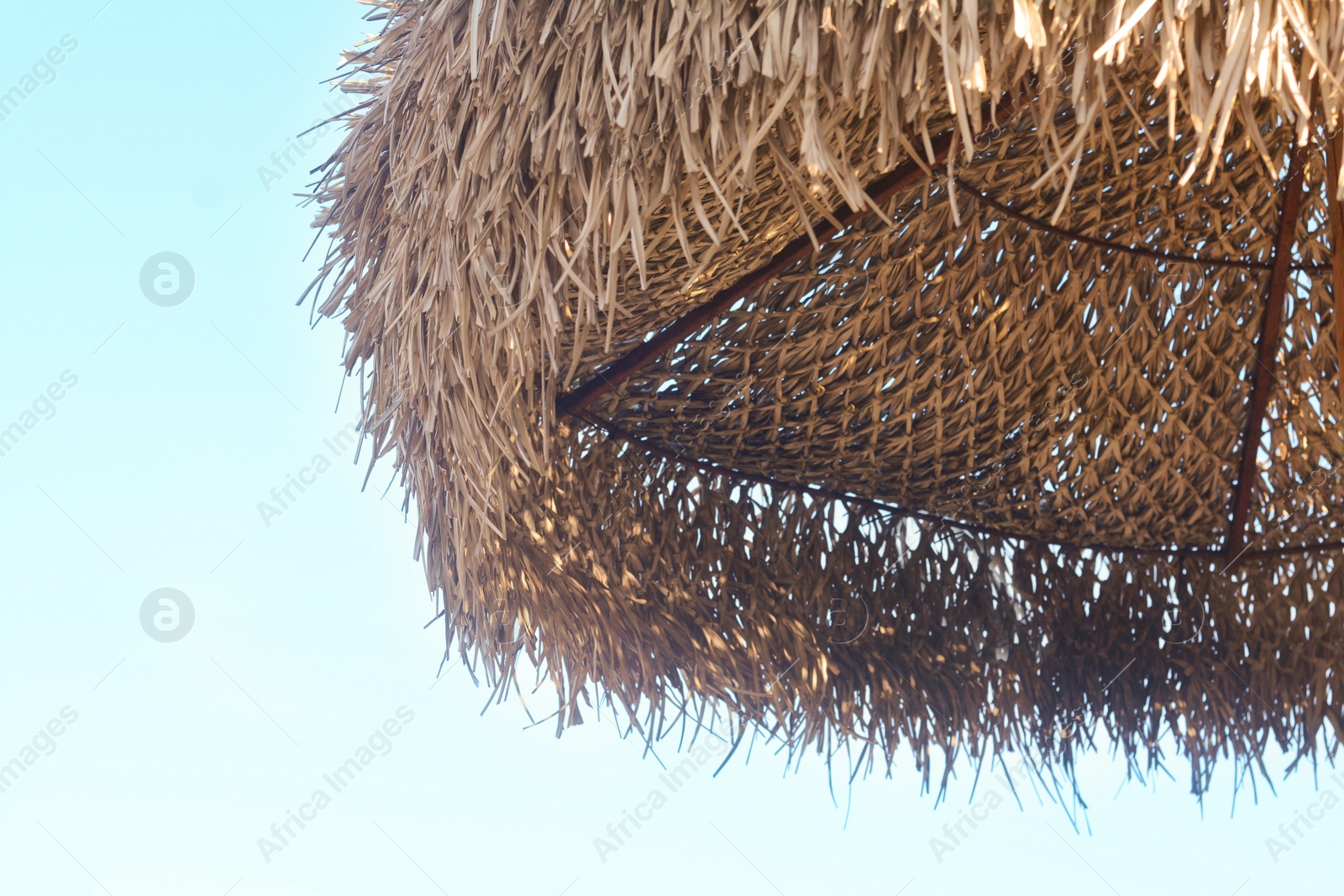 Photo of Beautiful straw beach umbrella against blue sky, closeup