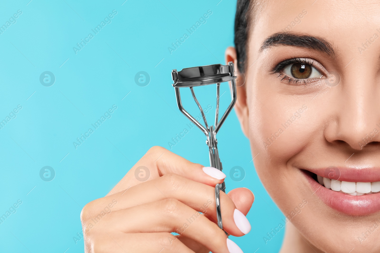 Photo of Beautiful young woman with eyelash curler on light blue background, closeup. Space for text