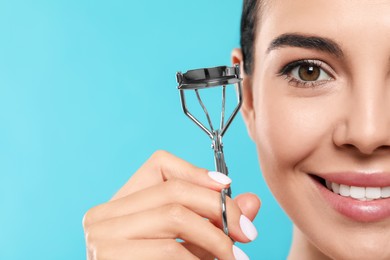 Beautiful young woman with eyelash curler on light blue background, closeup. Space for text