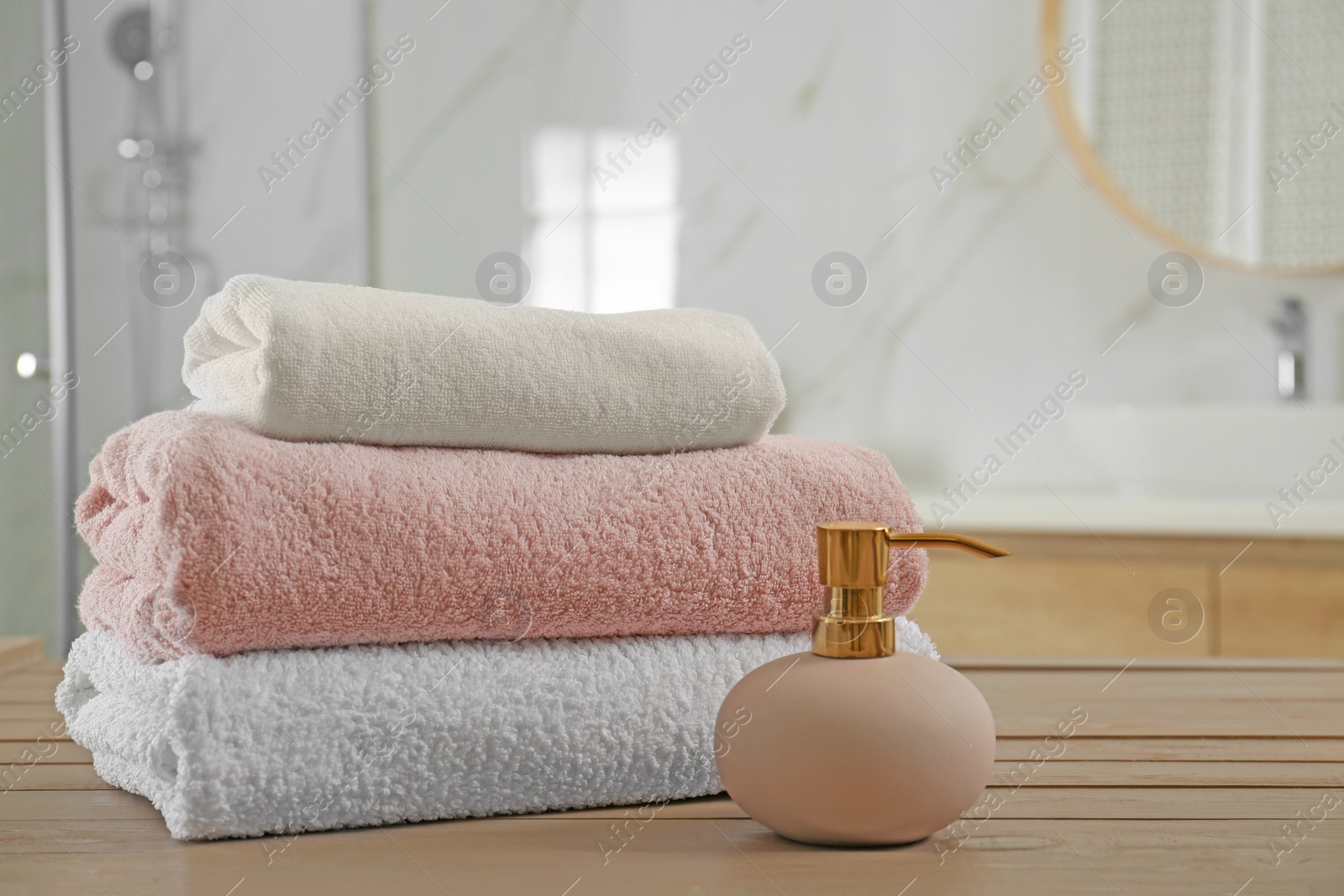 Photo of Stack of clean towels and soap dispenser on wooden table in bathroom