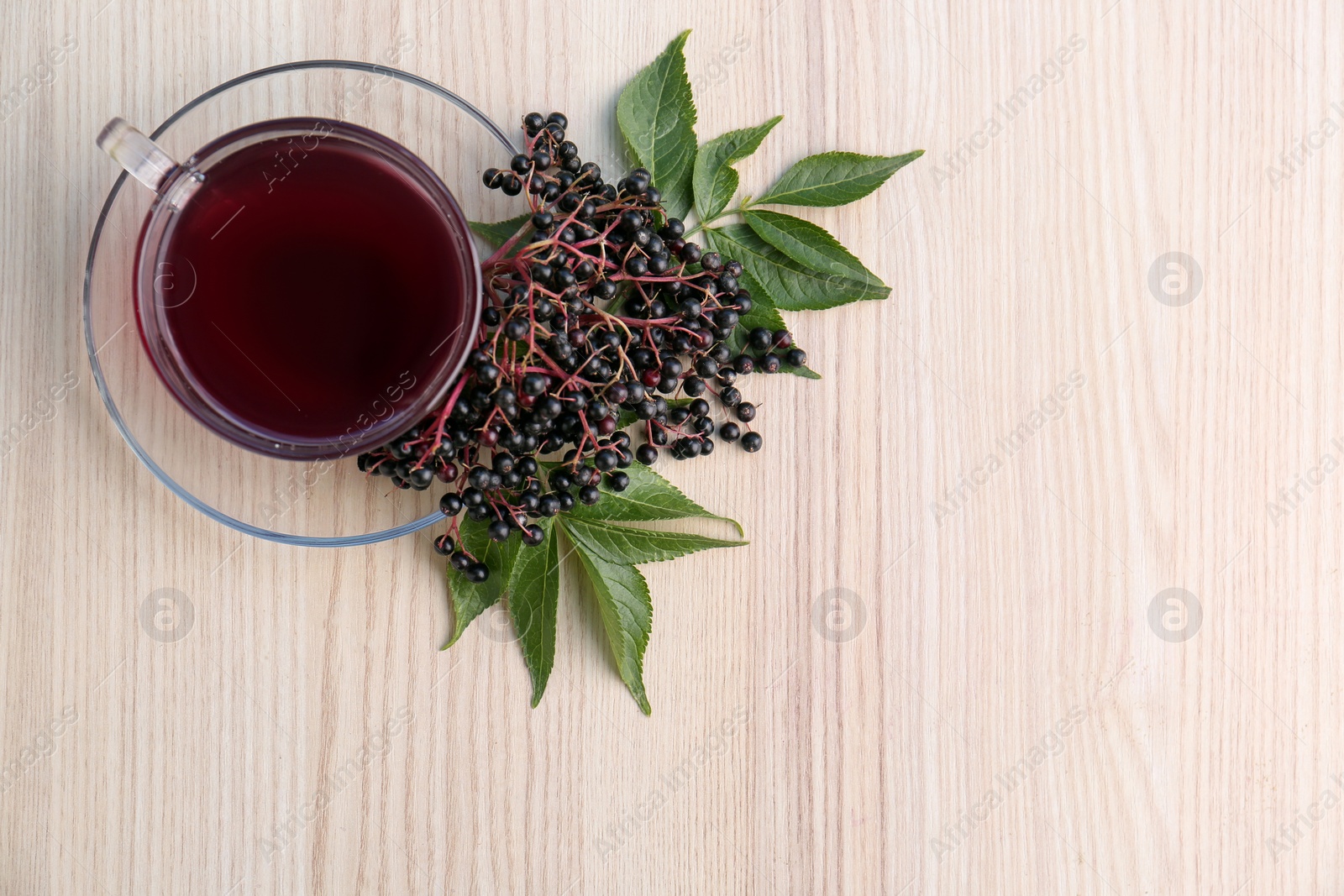 Photo of Glass cup of tasty elderberry tea and Sambucus berries on wooden table, top view. Space for text
