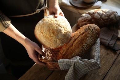 Photo of Man holding wicker basket with different types of bread at wooden table indoors, above view