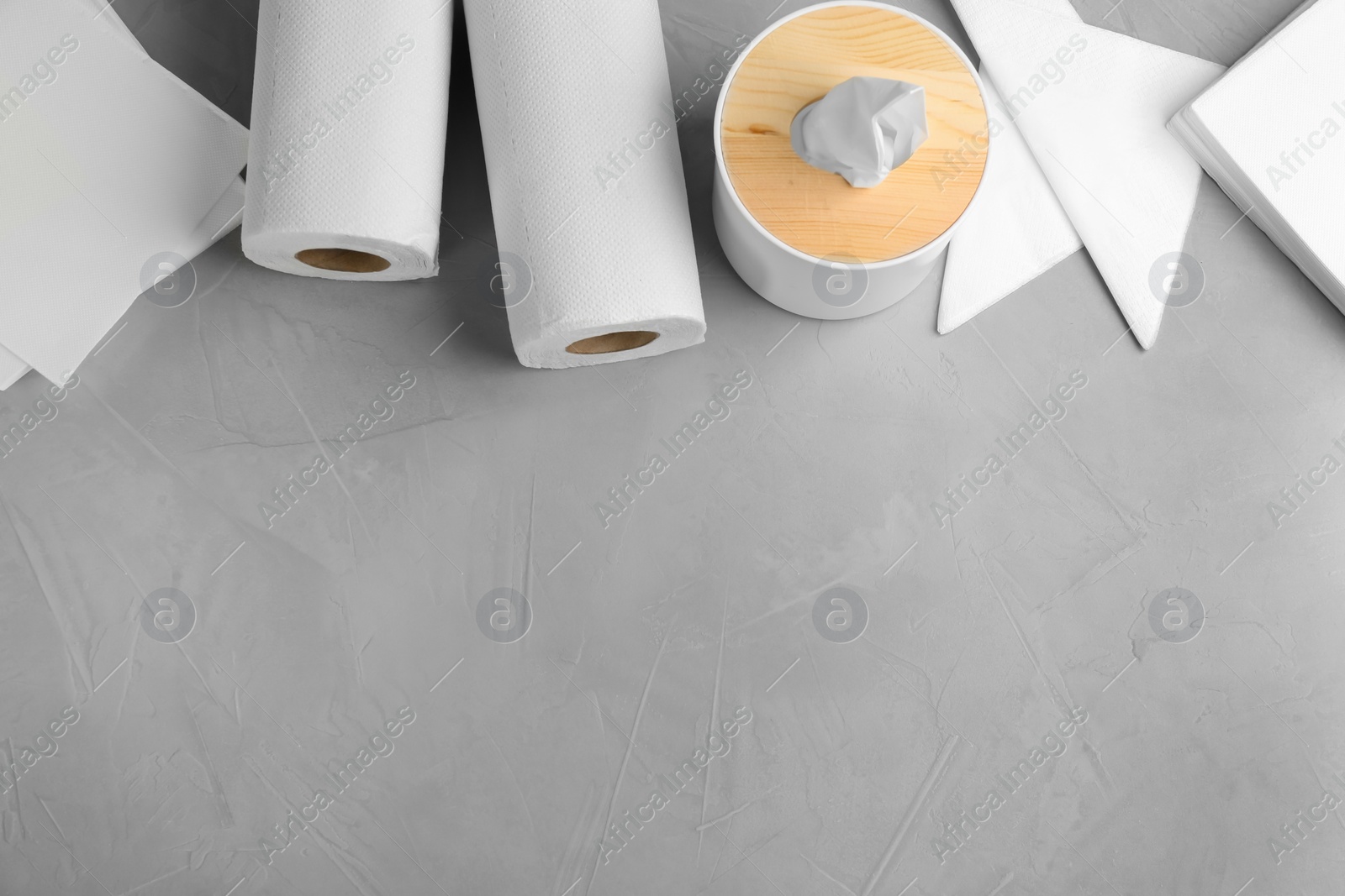 Photo of Clean napkins, box with tissues and rolls of paper towels on light table, flat lay. Space for text