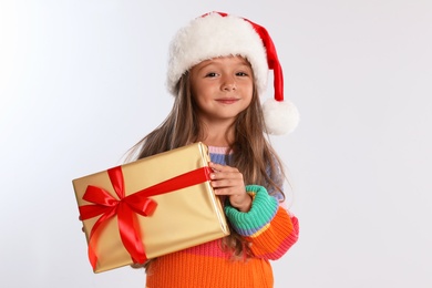 Photo of Happy little child in Santa hat with gift box on light grey background. Christmas celebration