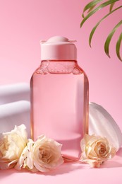 Photo of Bottle of micellar water, roses and cotton pads on pink background