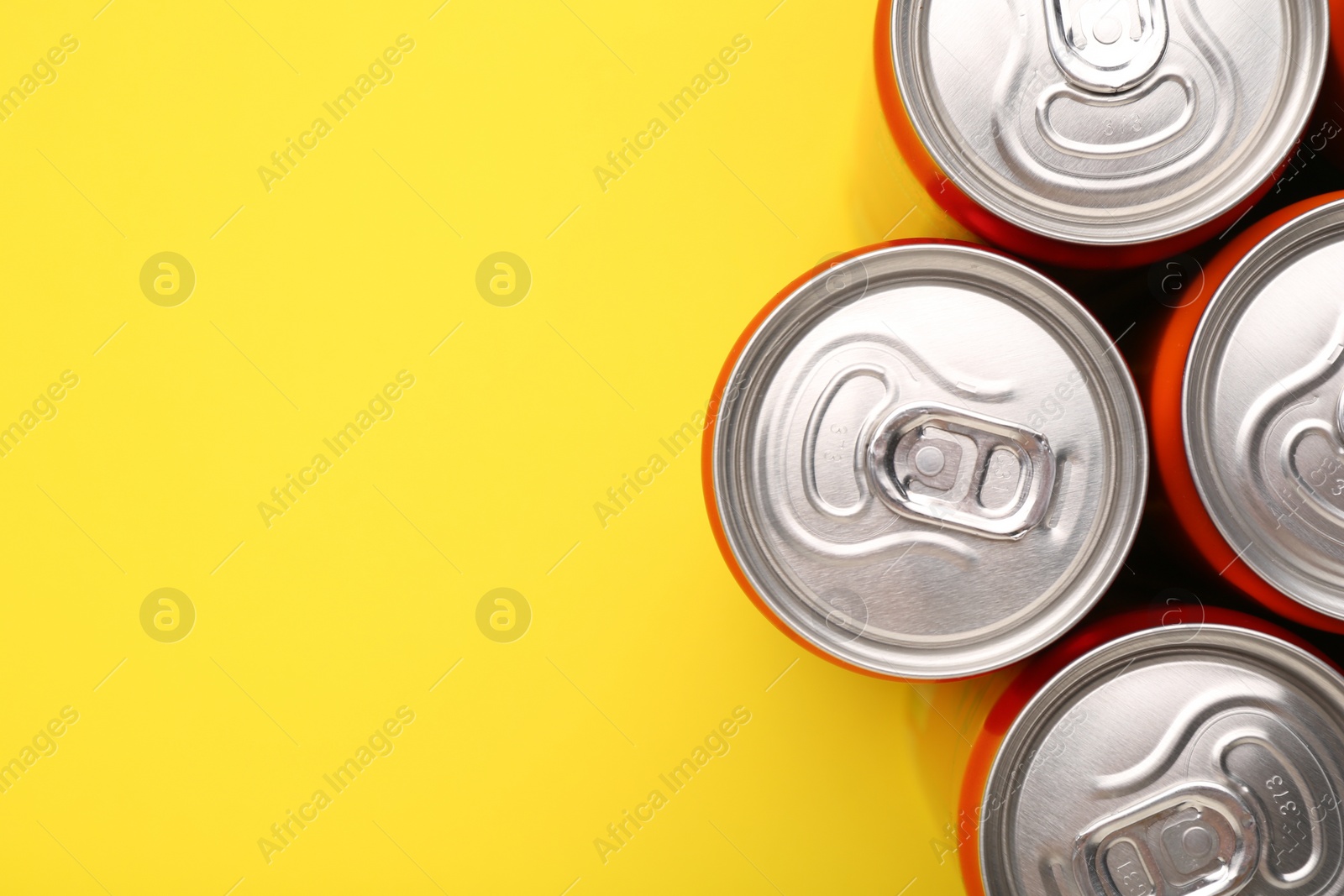 Photo of Energy drink in cans on yellow background, top view. Space for text