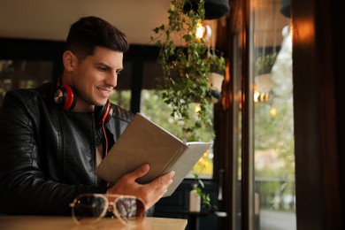 Man with headphones reading book at table in cafe