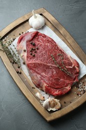 Wooden tray with piece of raw meat, garlic and thyme on grey table, top view