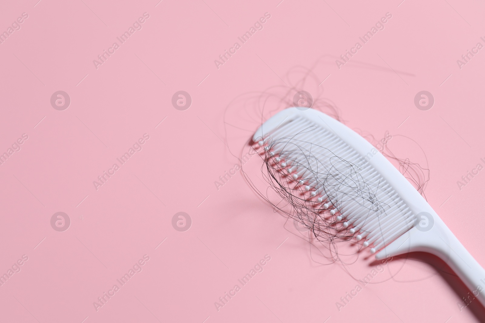 Photo of Comb with lost hair on pink background, space for text