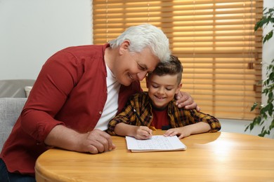 Photo of Little boy with his grandfather solving sudoku puzzle at table indoors