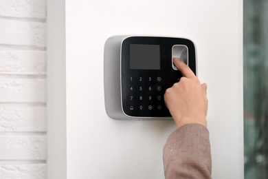 Photo of Woman scanning fingerprint on alarm system indoors, closeup