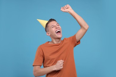 Happy young man in party hat on light blue background