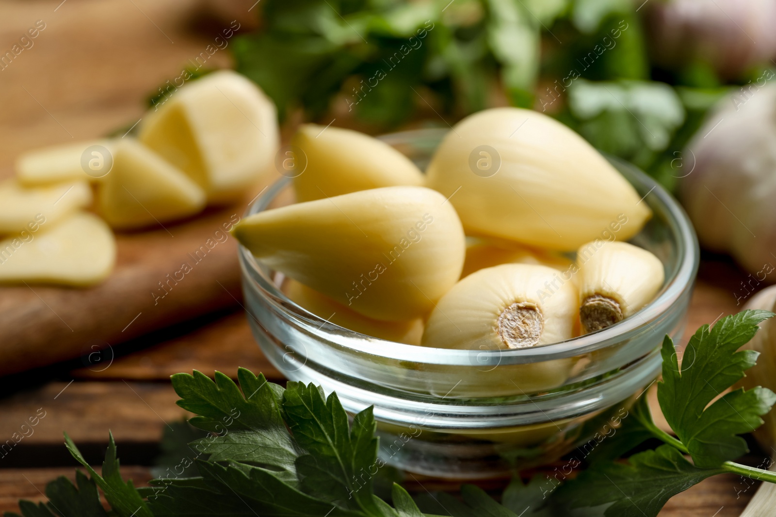 Photo of Fresh peeled garlic cloves in bowl and parsley on wooden table, closeup. Organic product