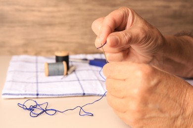 Photo of Closeup view of woman threading needle at beige table, space for text