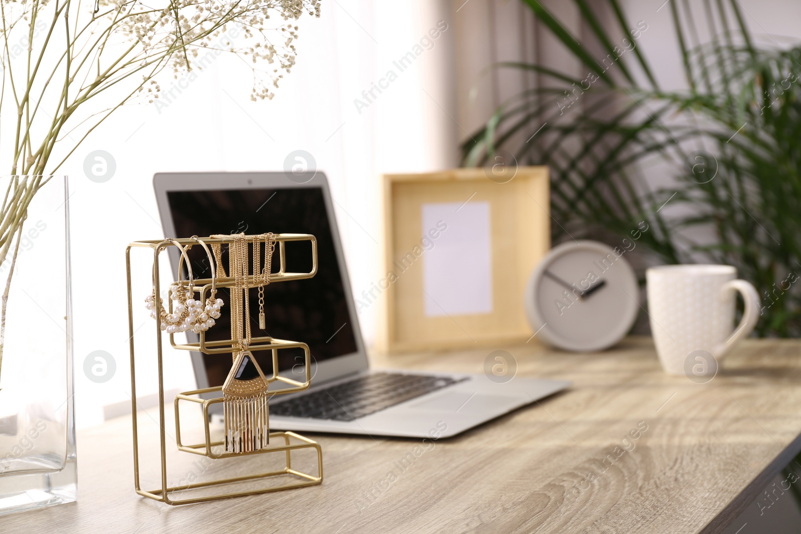 Photo of Stylish workplace interior with jewelry holder on wooden table near window. Space for text