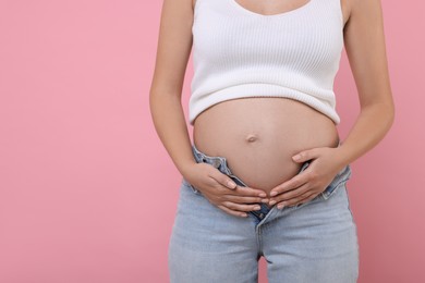 Photo of Pregnant woman in jeans on pink background, closeup. Space for text