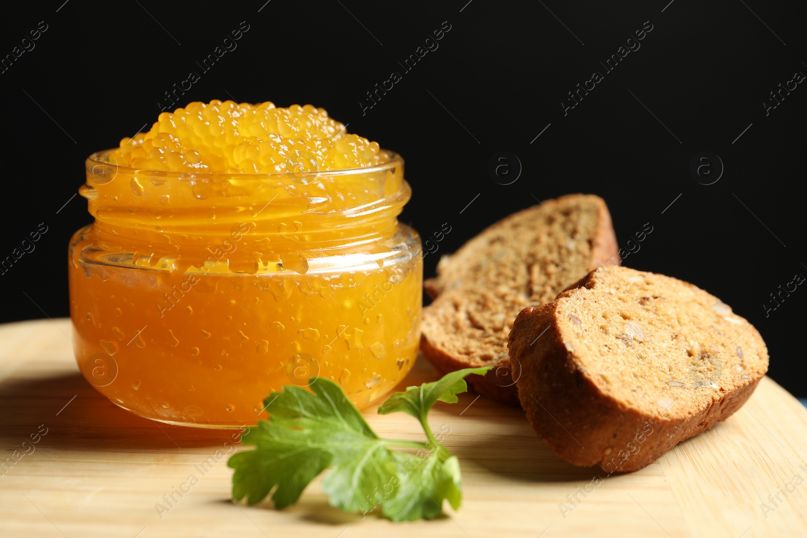 Photo of Fresh pike caviar in glass jar, bread and parsley on wooden board, closeup